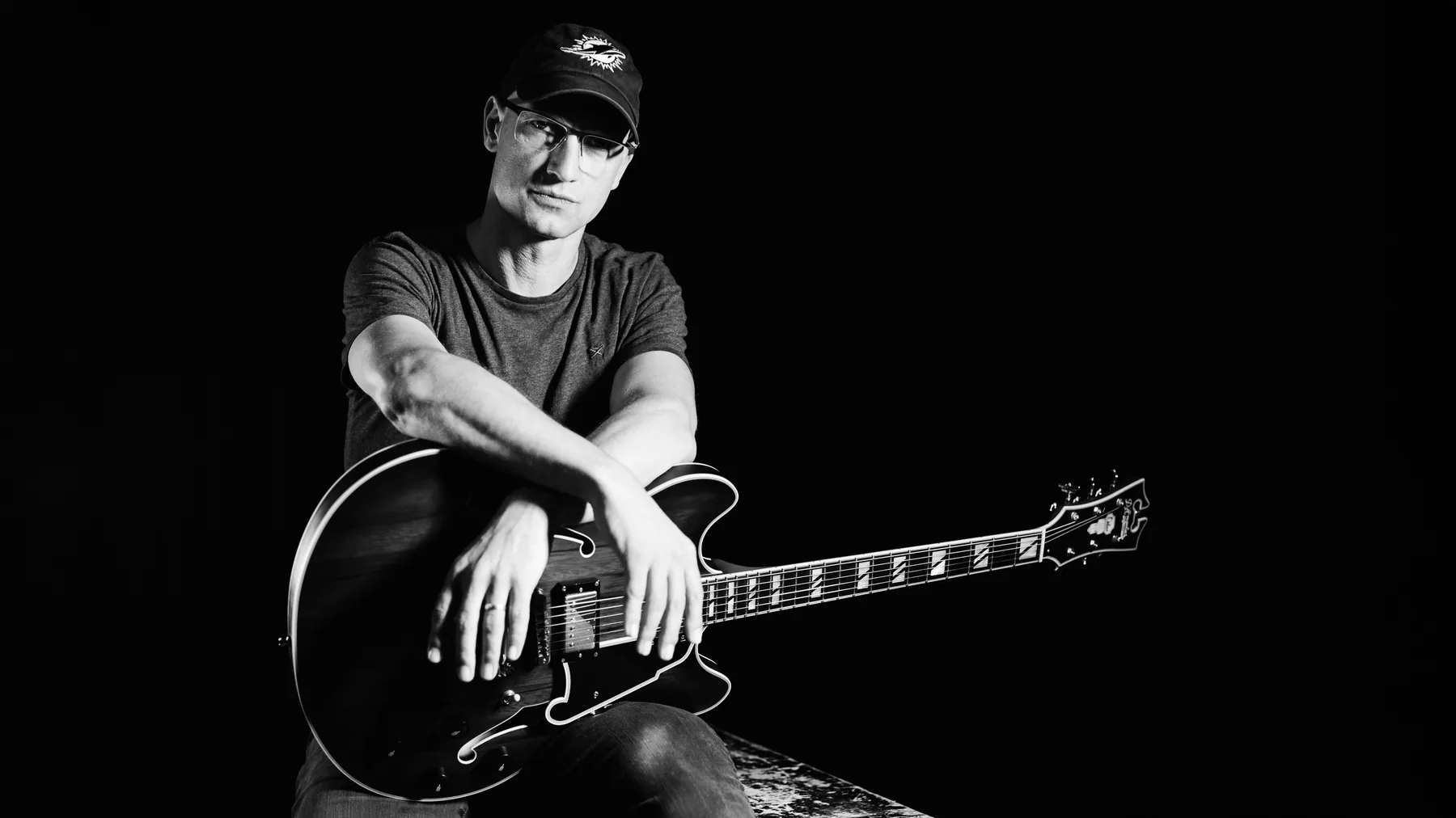 Pete Roth seated informally with his guitar in a black-and-white portrait.