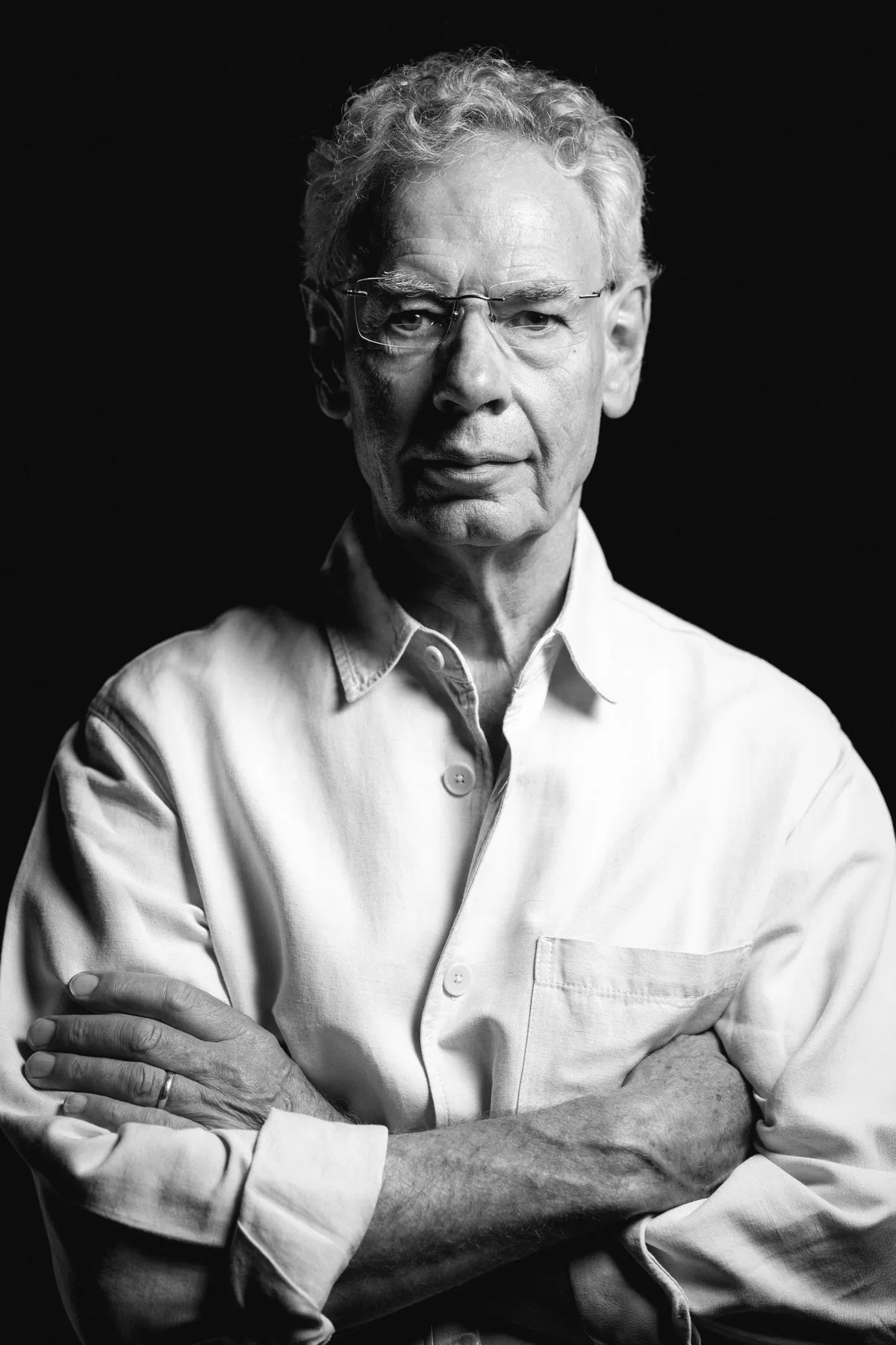 Black-and-white portrait of Bill Bruford standing with his arms folded.